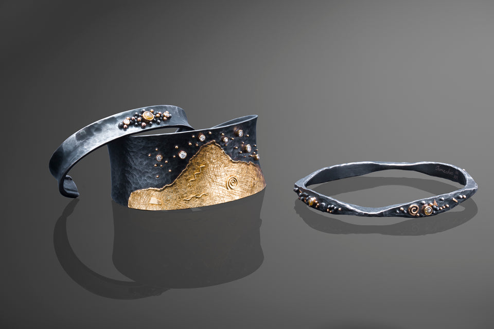 Mixed metal bracelets of silver and 18K yellow gold made with unique and custom designs. One bangle, one thick cuff and one thin cuff are included in the picture. Diamonds and gold accents are used throughout.