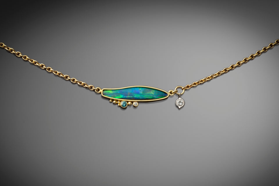 custom and unique necklace that includes a fiery Australian opal, several accent diamonds, and a diamond charm. This necklace is horizontally set and made with 14K yellow gold. 